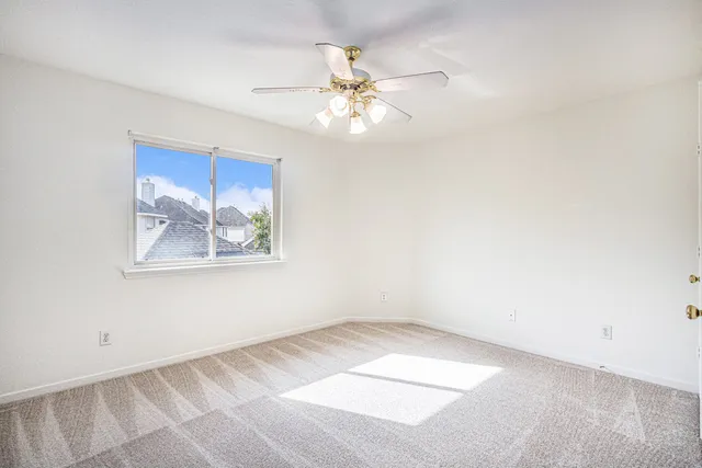 an empty room with a chandelier fan and windows