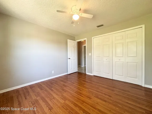 an empty room with wooden floor fan and windows