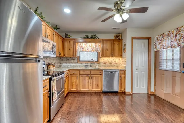 a kitchen with stainless steel appliances granite countertop a refrigerator a sink dishwasher a stove and white countertops with wooden floor