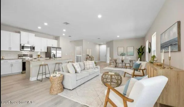 a living room with white couches and kitchen view with wooden floor