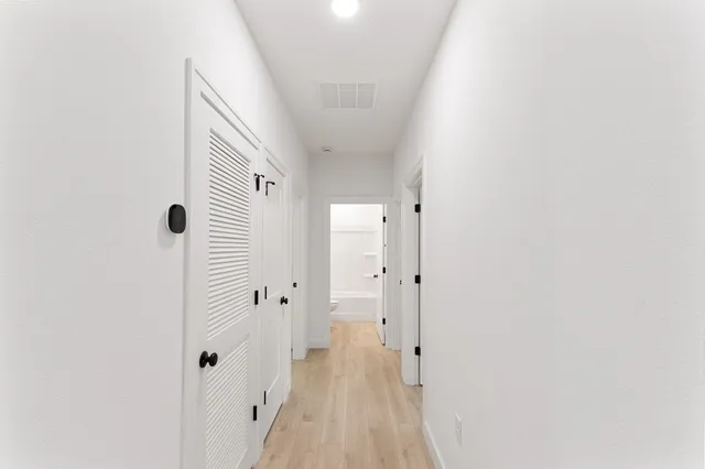 a view of a hallway with wooden floor and a bathroom