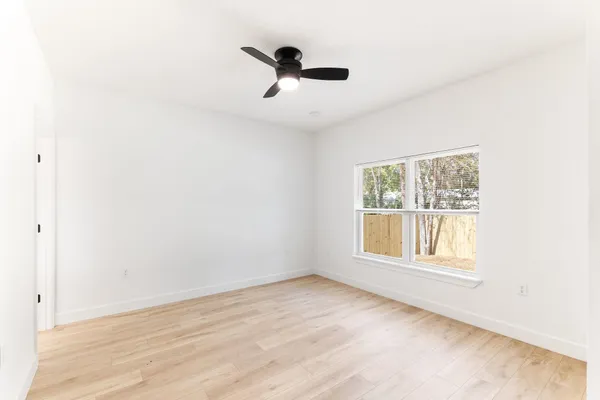 an empty room with wooden floor chandelier fan and windows