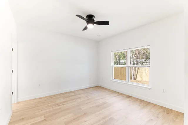 an empty room with wooden floor chandelier fan and windows