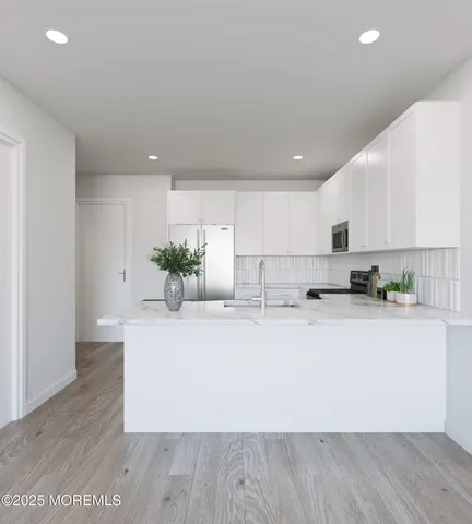 a large white kitchen with kitchen island a stove a sink a refrigerator and white cabinets with wooden floor