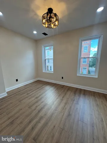 an empty room with wooden floor chandelier and windows