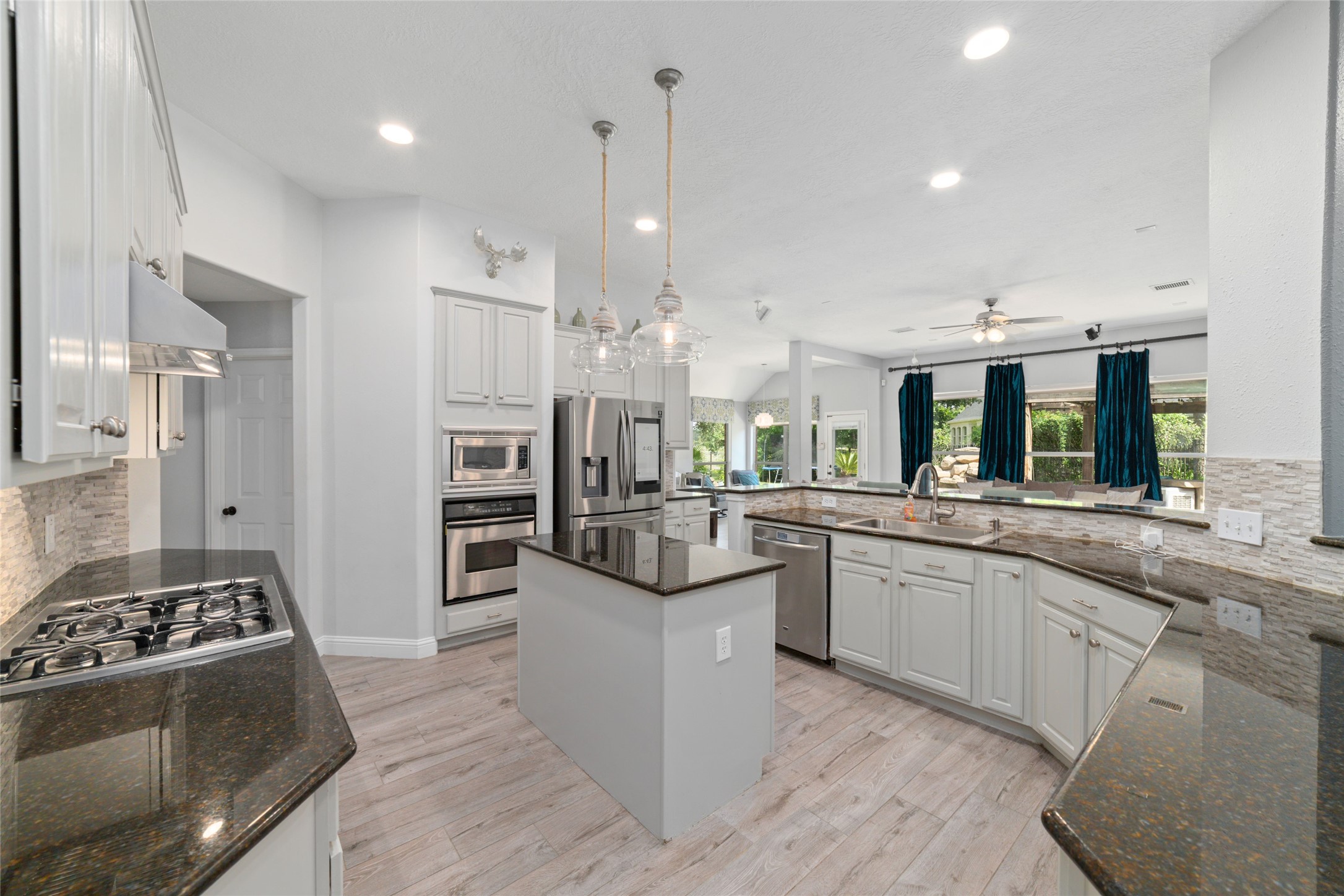24203 Moon Ridge Court Katy, TX 77494 - Photo 11 of 43 Modern kitchen features sleek granite countertops, stainless steel appliances, and an island with pendant lighting. The open layout connects to a bright living area with large windows and elegant flooring, creating a spacious and inviting atmosphere.