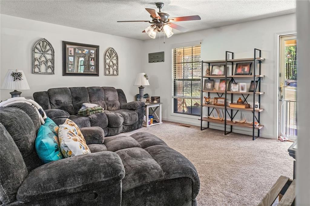 1024 Trail Street Valley, AL 36854 - Photo 11 of 37 Spacious living room featuring a comfortable sectional sofa, ceiling fan with integrated lighting, neutral carpet flooring, and an industrial-style shelving unit with open storage