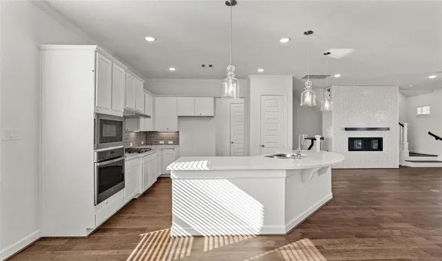a large kitchen with stainless steel appliances kitchen island granite countertop a stove a sink a refrigerator and white cabinets with wooden floor