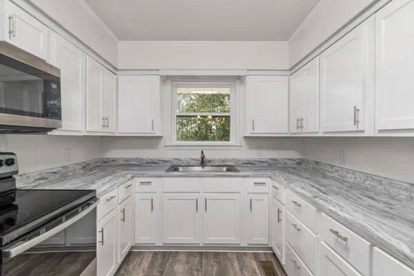 a kitchen with white cabinets appliances a sink and a window