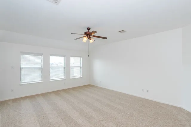 an empty room with chandelier fan and windows