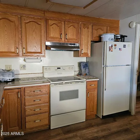 a white refrigerator freezer sitting inside of a kitchen with granite countertop wooden cabinets