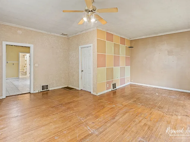 a view of an empty room with wooden floor and a ceiling fan