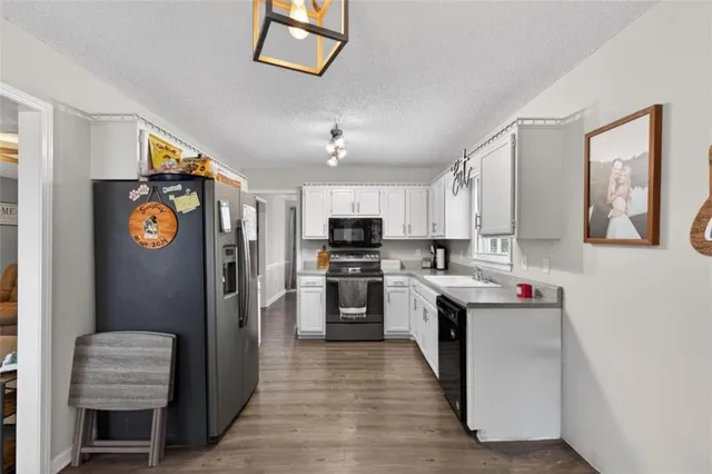 a kitchen with stainless steel appliances granite countertop a refrigerator a sink dishwasher a stove and white cabinets with wooden floor