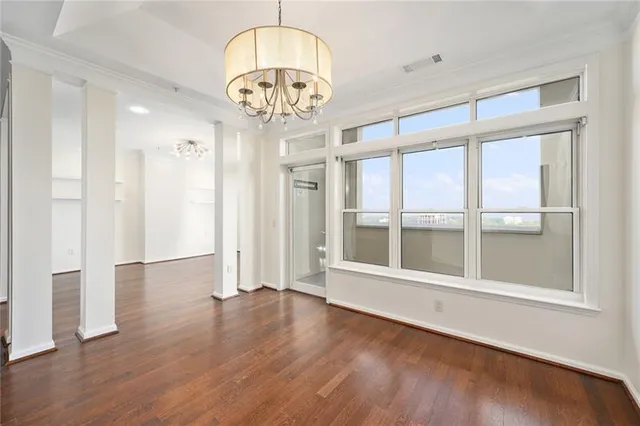 an empty room with wooden floor chandelier and windows