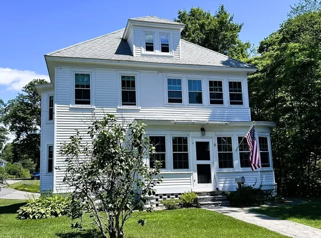 a view of a white house with large windows and a yard with plants and large trees