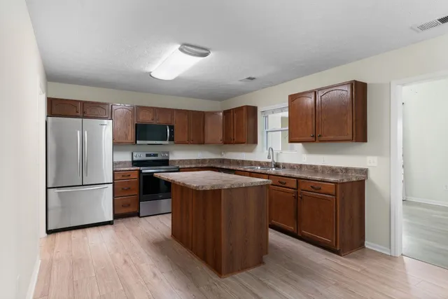 a kitchen with stainless steel appliances granite countertop wooden cabinets a refrigerator a sink a stove a microwave and wooden floors