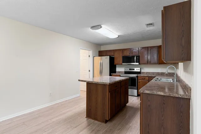 a kitchen with stainless steel appliances granite countertop a stove top oven a sink dishwasher and a refrigerator with wooden floor