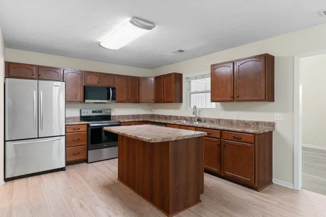 a kitchen with stainless steel appliances granite countertop a stove top oven a refrigerator and a sink with wooden floor