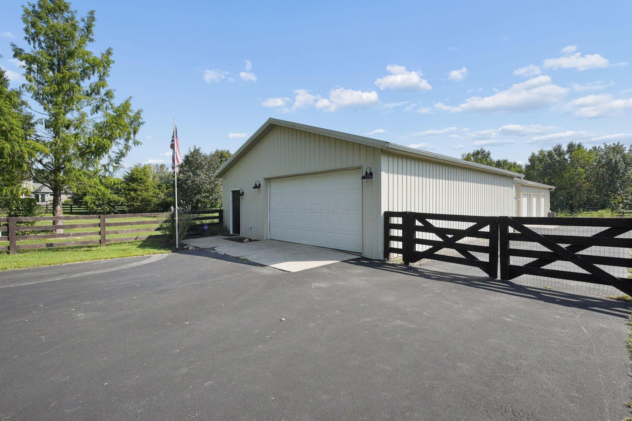 9435 Concord Road Powell, OH 43065 - Photo 50 of 77 Detached garage structure with a white overhead door, multiple exterior light fixtures, and a black fencing system