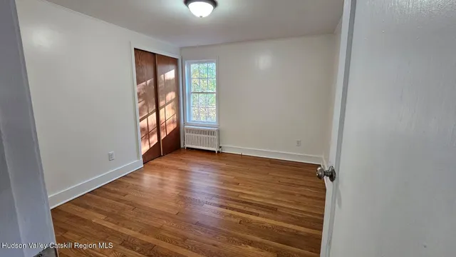 a view of an empty room with wooden floor and a window