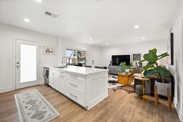 a large white kitchen with stainless steel appliances kitchen island granite countertop a living room view and wooden floor