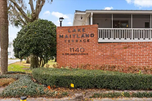 a view of a brick house with plants and large trees