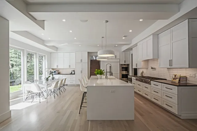 a kitchen with stainless steel appliances kitchen island granite countertop a stove top oven a sink a dining table and chairs with wooden floor