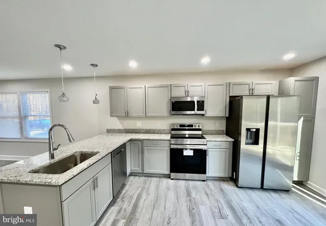 a kitchen with kitchen island granite countertop a stove top oven a sink and dishwasher a refrigerator with wooden floor