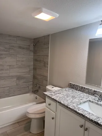 a bathroom with a granite countertop sink a toilet and bathtub