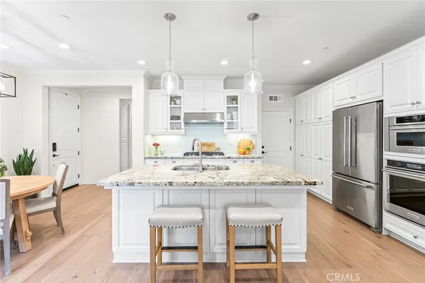 a kitchen with stainless steel appliances kitchen island granite countertop a dining table chairs and white cabinets