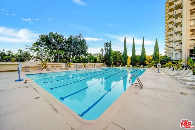 a view of a swimming pool with a bench and trees in the background