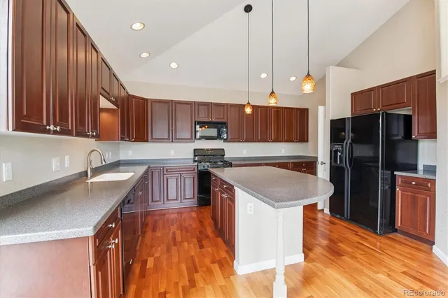 a kitchen with stainless steel appliances granite countertop a sink a stove a refrigerator and island with wooden floor