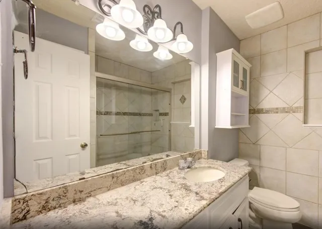 a bathroom with a granite countertop sink mirror vanity and toilet