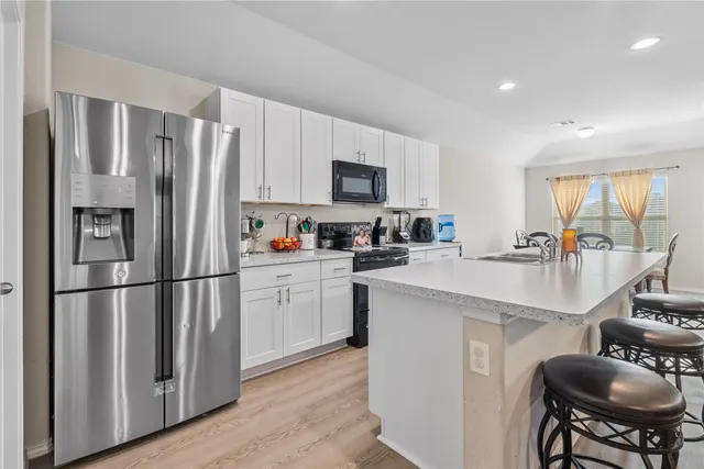 a kitchen with stainless steel appliances granite countertop a refrigerator a stove a sink a dining table and chairs with wooden floor