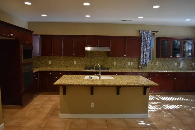 a kitchen with kitchen island granite countertop a sink a counter top space and cabinets