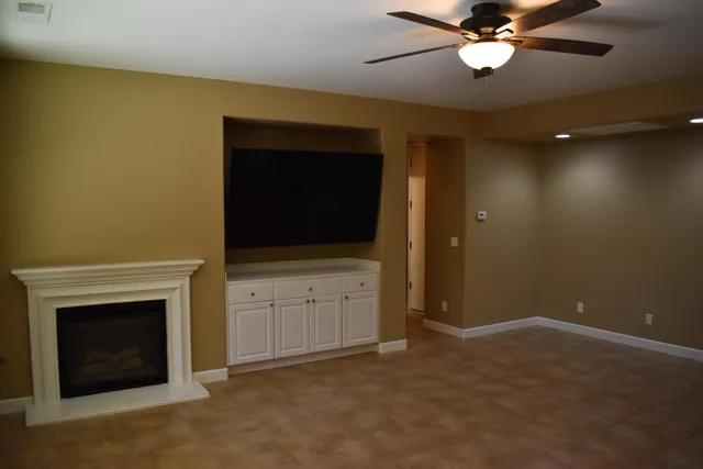 a view of an empty room with a fireplace and a ceiling fan