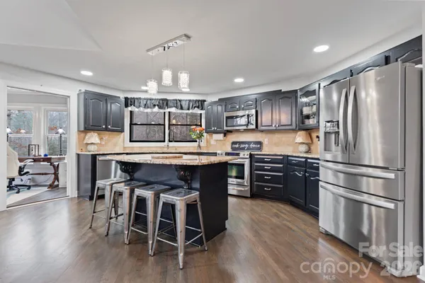 a kitchen with stainless steel appliances granite countertop a refrigerator a stove a sink a dining table and chairs with wooden floor