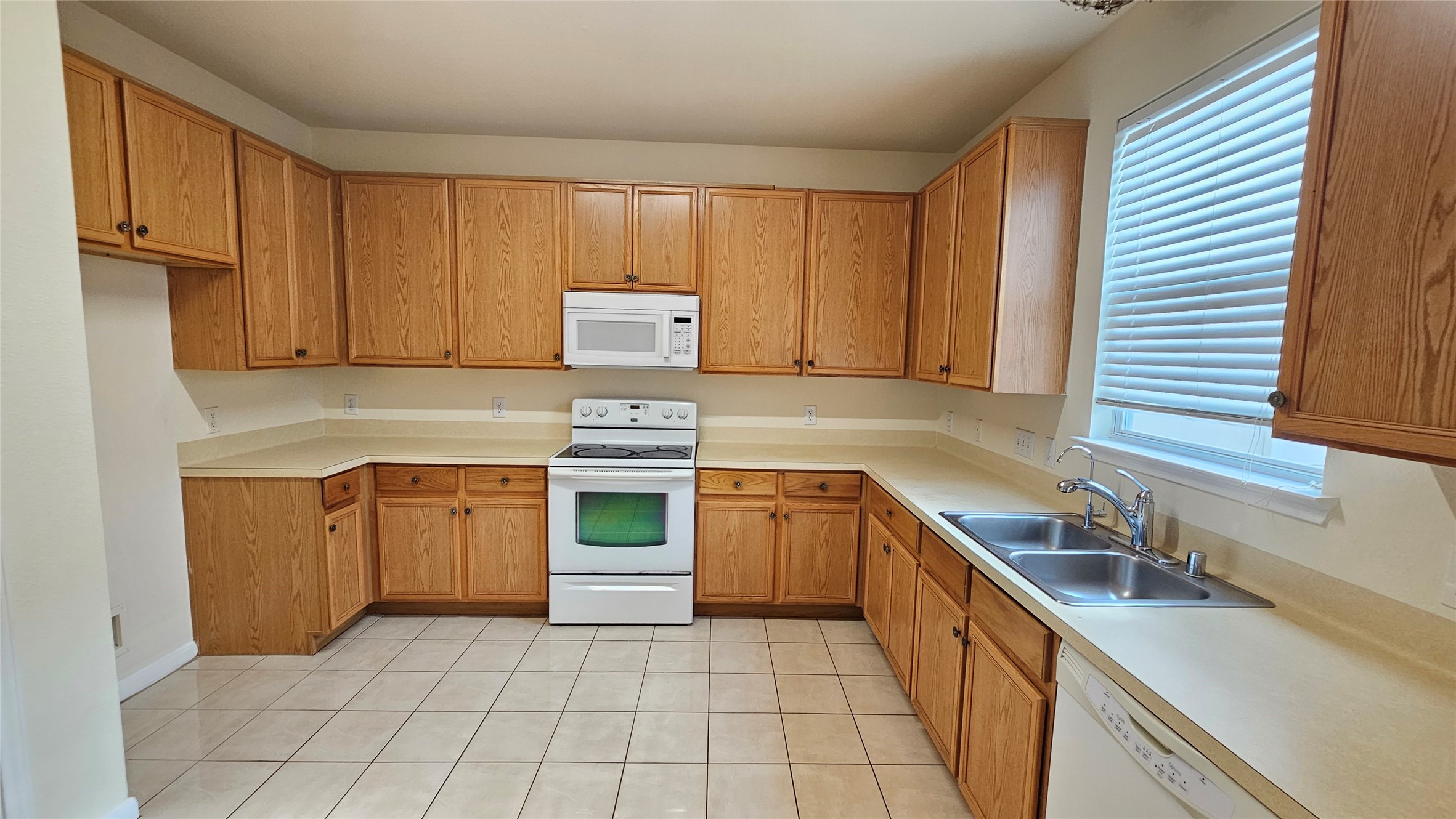 7918 Barnes Ridge Lane Houston, TX 77072 - Photo 7 of 34 This spacious kitchen features ample wooden cabinetry, a white stove and microwave, dual sinks, and a dishwasher. It has a tiled floor and a bright window, creating a functional and inviting cooking space.
