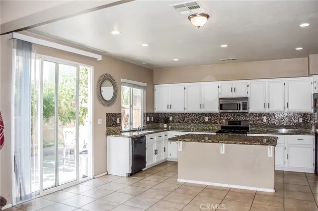 a kitchen with stainless steel appliances granite countertop a stove top oven a sink a refrigerator and white cabinets