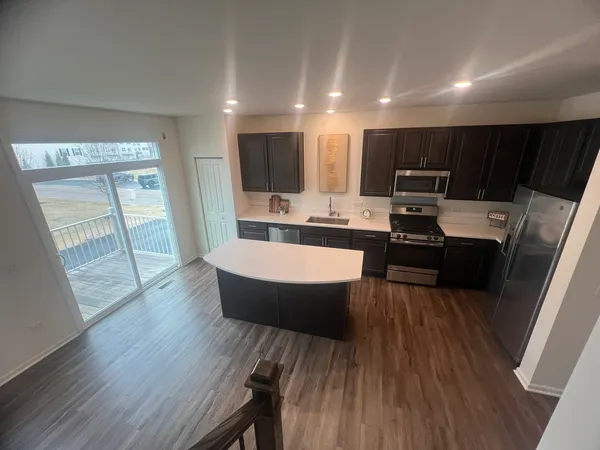 a living room with stainless steel appliances a dining table wooden floor and a large window