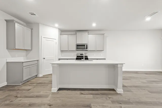 a white kitchen with granite countertop a stove top oven a sink and white cabinets with wooden floor