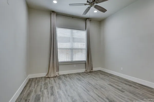 an empty room with wooden floor a ceiling fan and windows