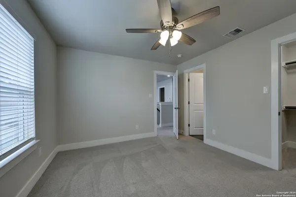 an empty room with chandelier fan and windows