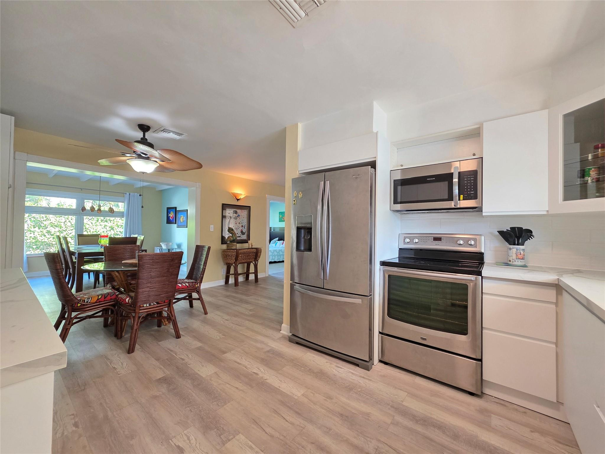 2585 Southeast 3rd Street Pompano Beach, FL 33062 - Photo 16 of 71 a kitchen with stainless steel appliances granite countertop a stove top oven a refrigerator a dining table and chairs with wooden floor