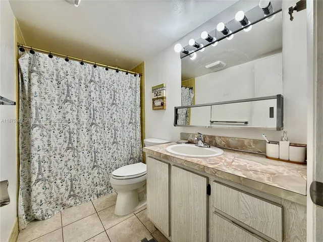 a bathroom with a granite countertop sink a toilet a mirror and shower curtain