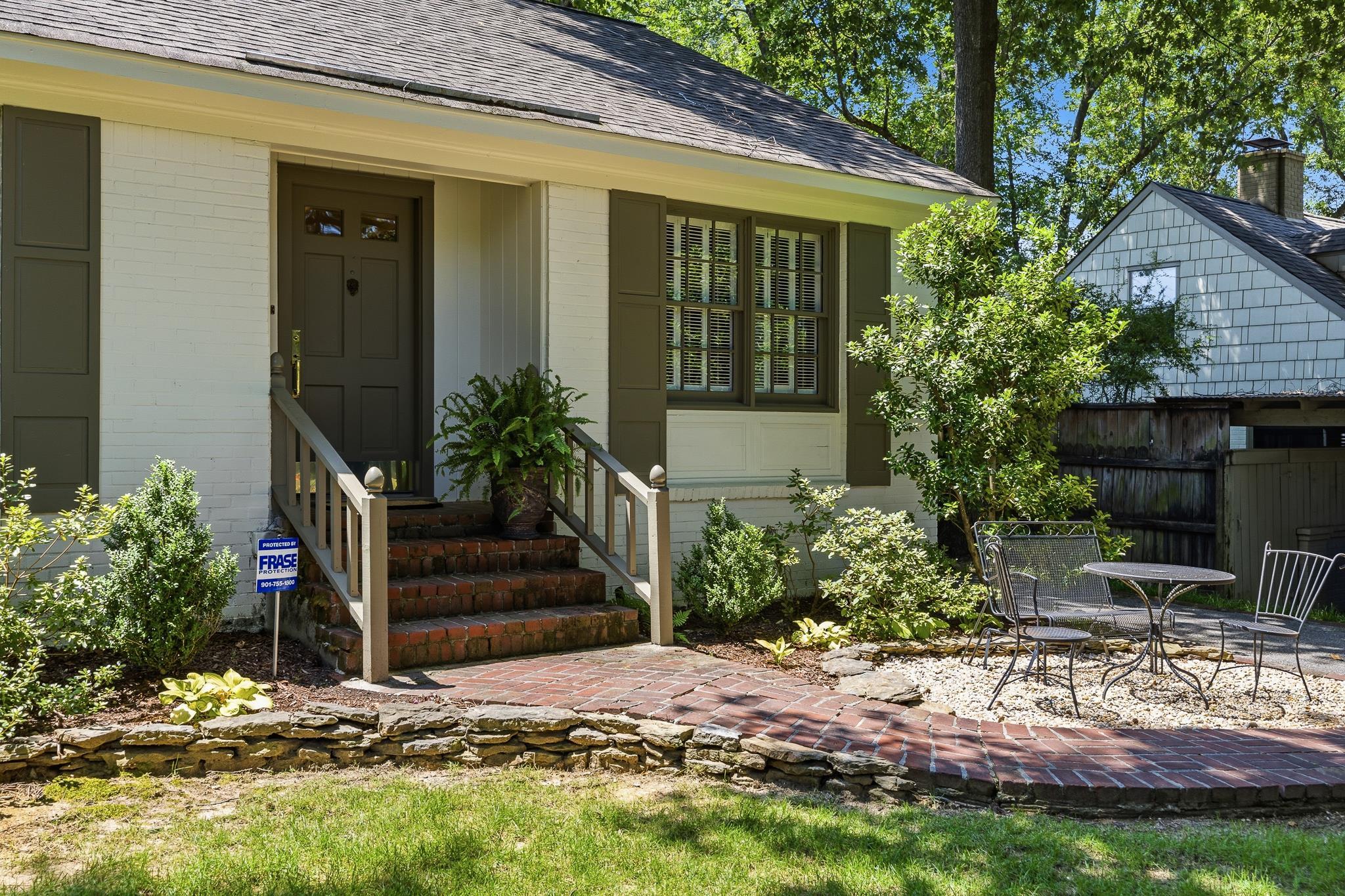 White brick exterior with dark shutters, featuring a prominent front entrance with brick steps and a wood handrail