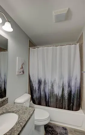 a bathroom with a granite countertop sink a toilet a mirror and shower curtain