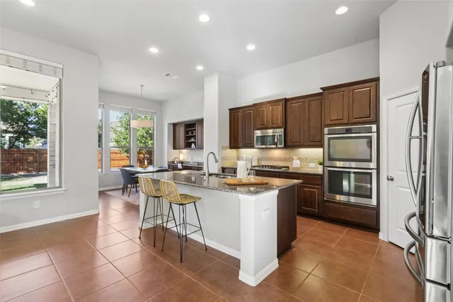 a kitchen with stainless steel appliances granite countertop a stove top oven a sink dishwasher a dining table and chairs with wooden floor