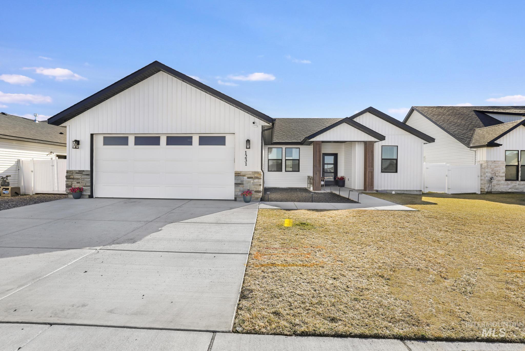 Modern farmhouse style home featuring a gate, driveway, a garage, and stone siding