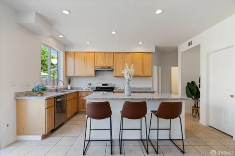 a kitchen with stainless steel appliances granite countertop wooden cabinets a stove top oven a sink a dining table and chairs